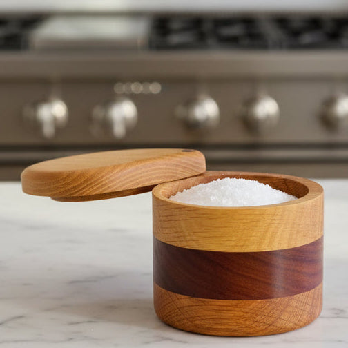 Wooden container with a lid filled with salt on a light gray background