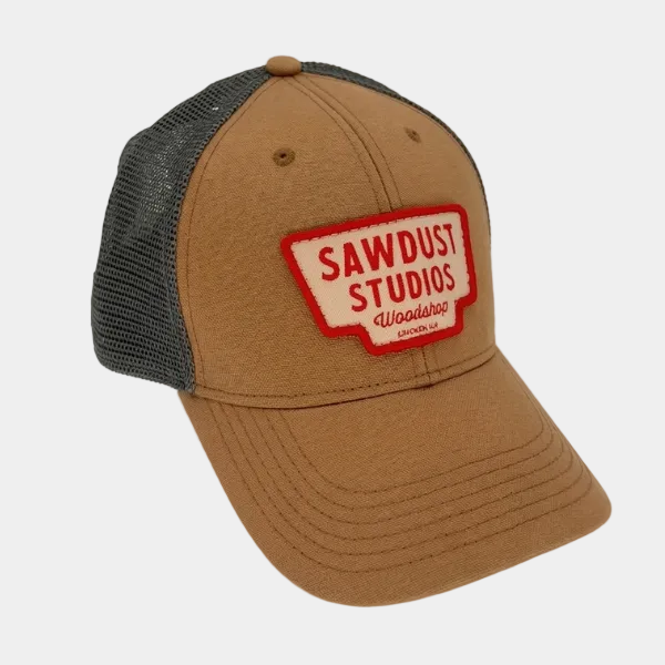 Brown trucker cap with red and white 'Sawdust Studios' logo on a light gray background
